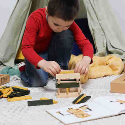 Enfant réalisant une construction avec des planchettes Kapla vertes et jaunes