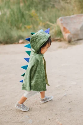 Enfant portant la cape de dragon verte Great Pretenders avec pointes dorsales bleues