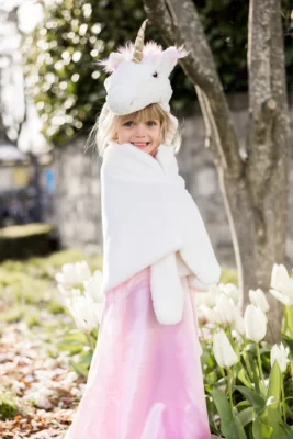 Enfant portant la cape licorne blanche Great Pretenders en extérieur parmi des fleurs
