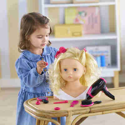 Enfant réalisant une coiffure sur la tête à coiffer Corolle