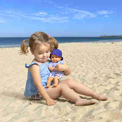 Enfant tenant le poupon Bébé Bain Marin Corolle sur la plage