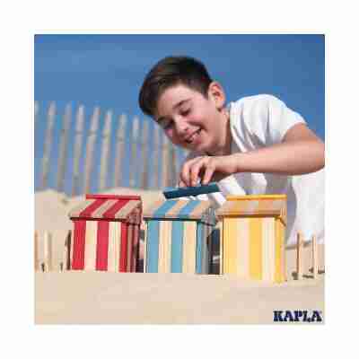 Enfant construisant trois cabanes avec des planchettes Kapla rouges bleues jaunes et naturelles