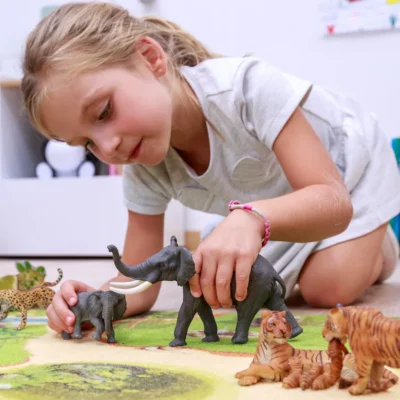 Enfant jouant avec la figurine Éléphant Papo entourée de figurines d’animaux sauvages