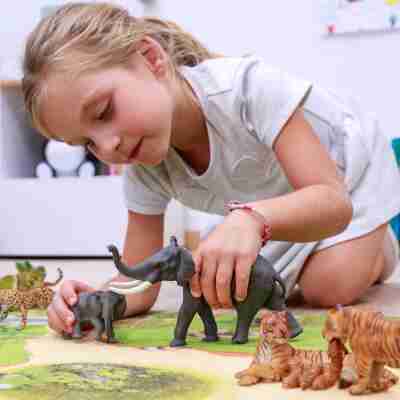 Enfant jouant avec la figurine Éléphant Papo entourée de figurines d’animaux sauvages