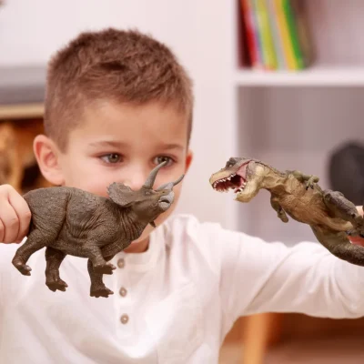 Enfant jouant avec une figurine Tricératops Papo face à un dinosaure carnivore